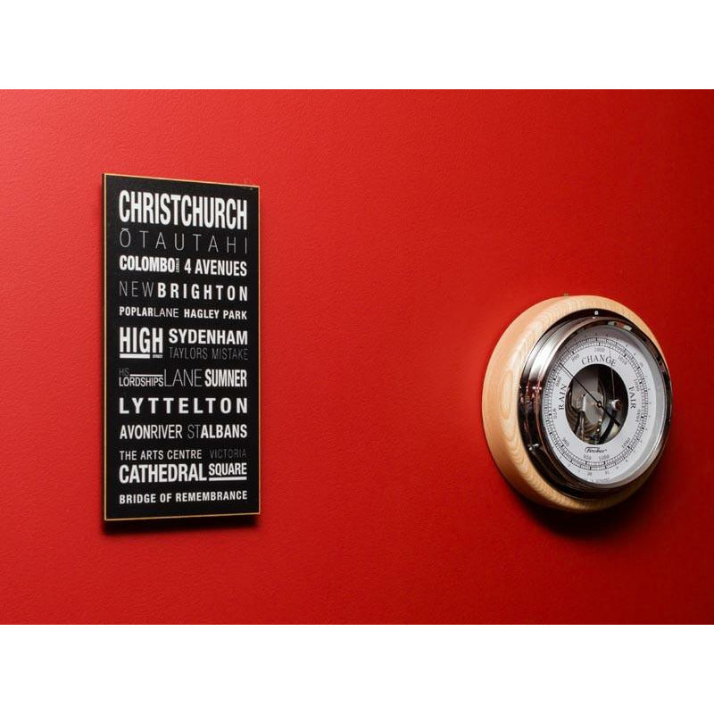 Wood-framed barometer with dial on red wall, beside black and white city typography art