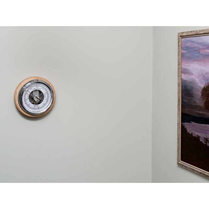 Wall-mounted German barometer with wooden frame next to a framed painting indoors