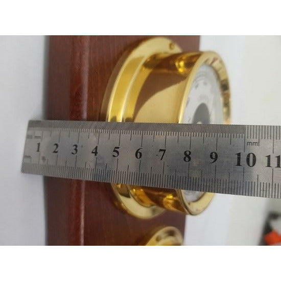 Gold nautical barometer mounted on wood being measured with a metal ruler in centimeters