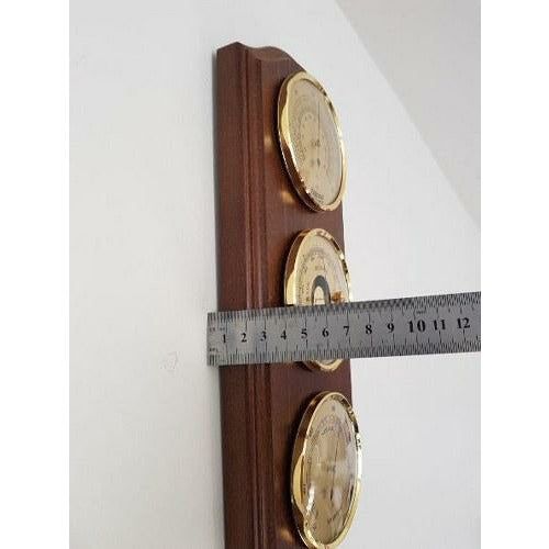 Triple gold dial weather station with barometer, hygrometer, and thermometer on wood panel measured by ruler