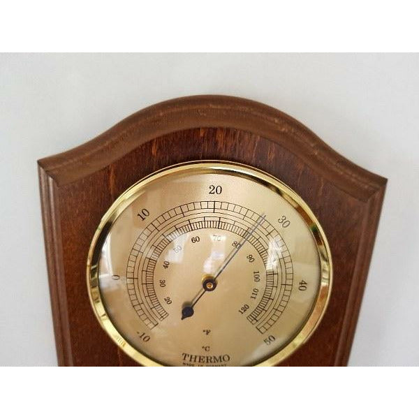 Wall-mounted analog thermometer with gold trim on wood plaque, displaying Celsius and Fahrenheit scales