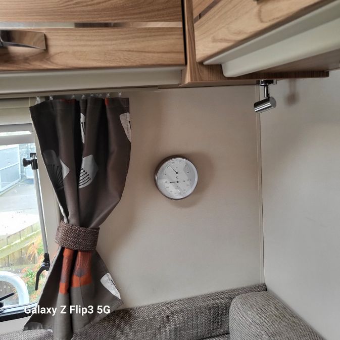 RV interior wall with mounted round hygrometer and thermometer, curtain, and seating area